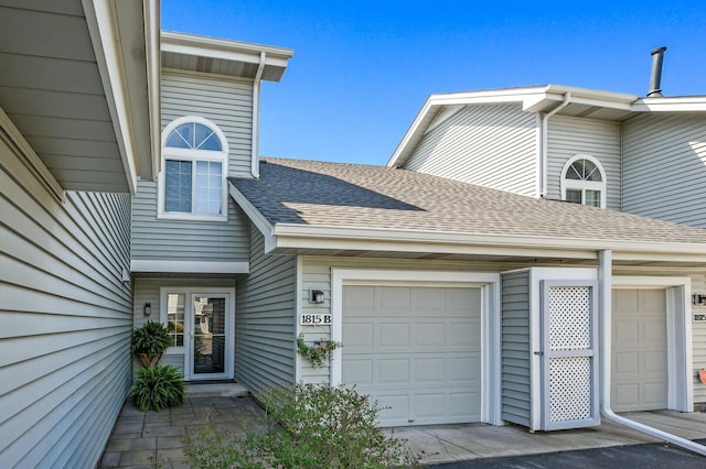 entrance to property with roof with shingles, a garage, and driveway
