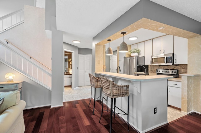 kitchen featuring appliances with stainless steel finishes, a kitchen breakfast bar, white cabinetry, decorative light fixtures, and decorative backsplash