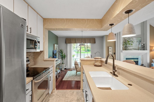 kitchen featuring appliances with stainless steel finishes, a sink, white cabinetry, hanging light fixtures, and light countertops