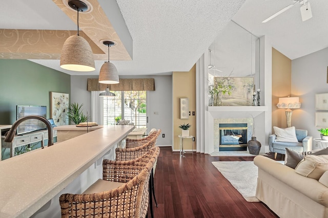 dining area featuring ceiling fan, dark wood finished floors, a tile fireplace, baseboards, and vaulted ceiling