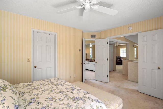 bedroom with light carpet, wallpapered walls, a textured ceiling, and ceiling fan