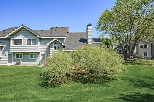 back of property with a yard, a shingled roof, and a chimney