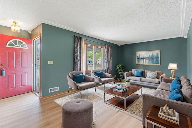 living area with a textured ceiling, light wood-type flooring, ornamental molding, and baseboards