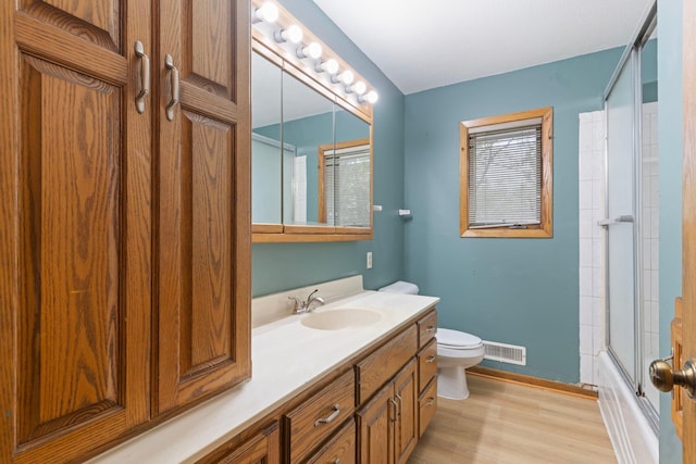 bathroom featuring toilet, baseboards, wood finished floors, vanity, and shower / bath combination with glass door