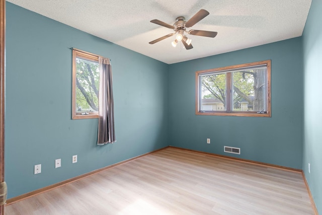 spare room featuring healthy amount of natural light, wood finished floors, a ceiling fan, a textured ceiling, and baseboards