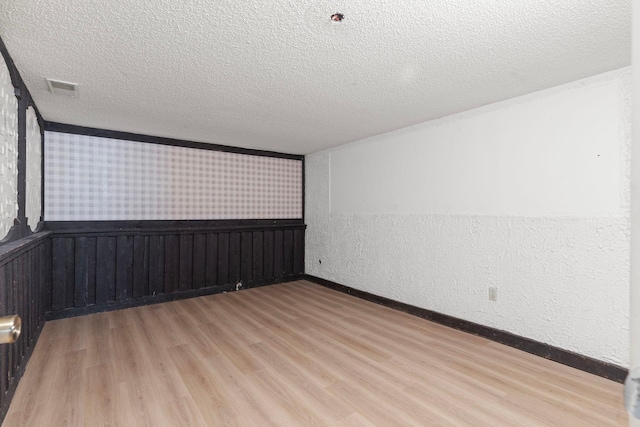 spare room featuring a textured ceiling, wood finished floors, and a wainscoted wall