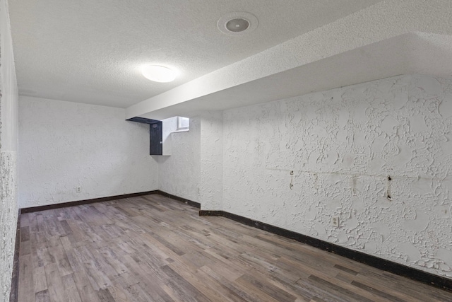 finished below grade area featuring a textured ceiling, a textured wall, wood finished floors, and baseboards