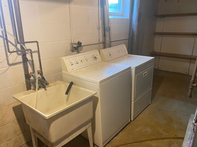 clothes washing area with washer and clothes dryer, concrete block wall, and a sink