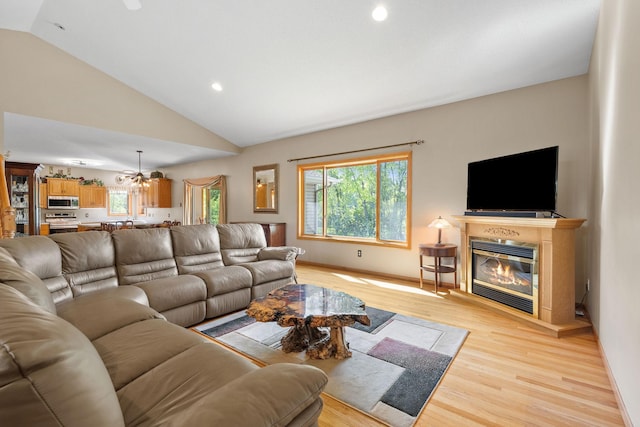 living room featuring a chandelier, vaulted ceiling, light wood-type flooring, a glass covered fireplace, and recessed lighting