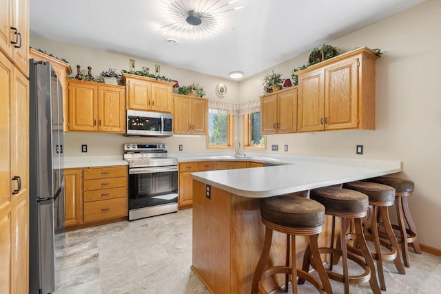 kitchen featuring appliances with stainless steel finishes, a peninsula, a breakfast bar area, light countertops, and a sink