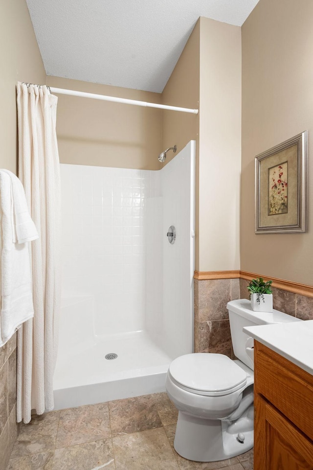 bathroom featuring tile walls, toilet, curtained shower, vanity, and wainscoting