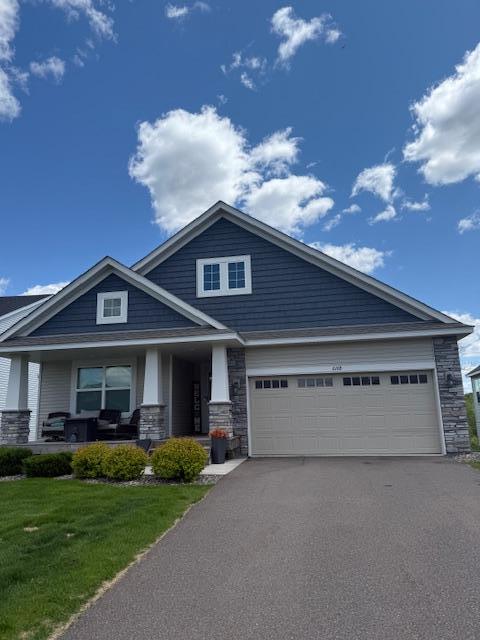 6168 Quenroe Ave NE, Otsego, MN 55330 - craftsman-style home with asphalt driveway, a front lawn, an attached garage, covered porch, and stone siding