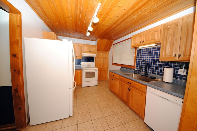 kitchen with white appliances, a sink, rail lighting, dark countertops, and under cabinet range hood