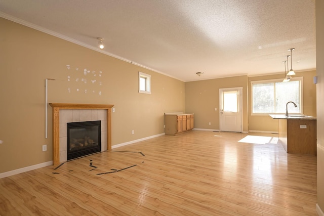 unfurnished living room featuring crown molding, plenty of natural light, a fireplace, light wood-type flooring, and a sink