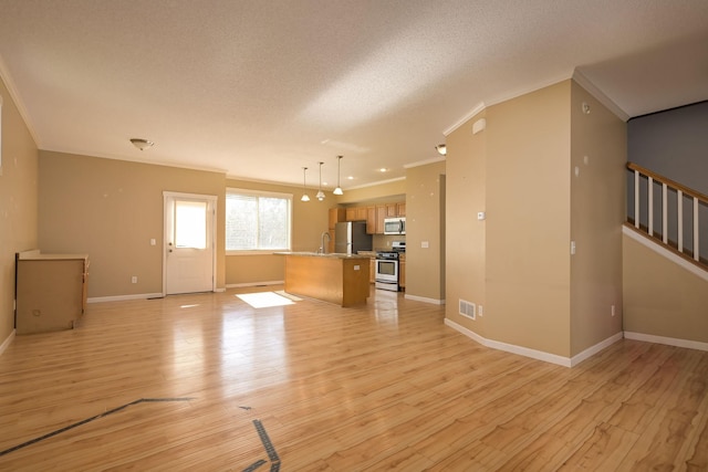 unfurnished living room featuring ornamental molding, a sink, light wood-style floors, baseboards, and stairway