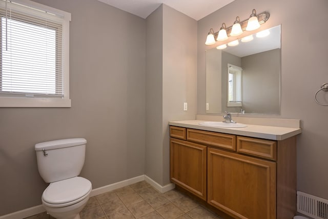 half bathroom with toilet, vanity, baseboards, and tile patterned flooring