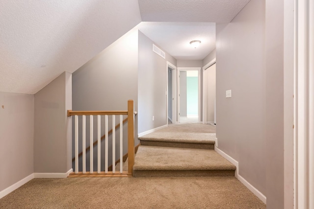 stairway with carpet, a textured ceiling, lofted ceiling, and baseboards