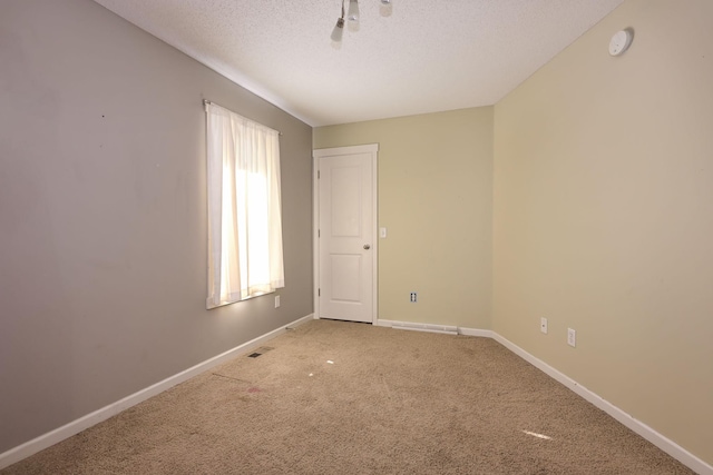 carpeted empty room featuring a textured ceiling, baseboards, and a smoke detector