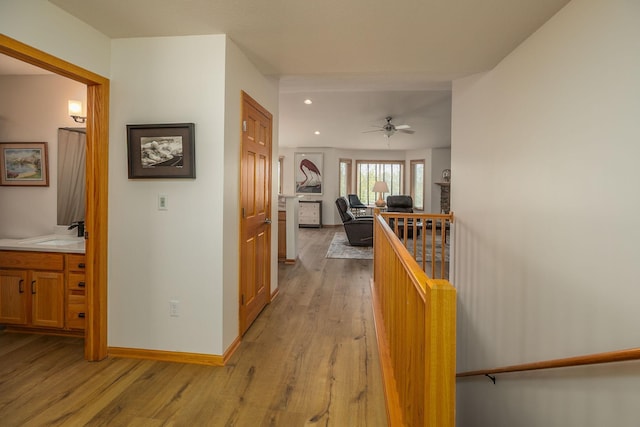 hallway with an upstairs landing, light wood-style flooring, recessed lighting, a sink, and baseboards