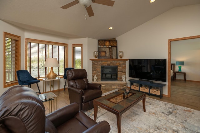 living area featuring vaulted ceiling, baseboards, a ceiling fan, wood finished floors, and a stone fireplace