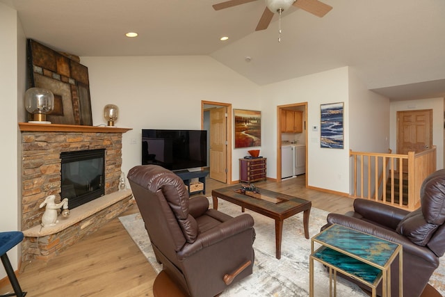 living area featuring washing machine and clothes dryer, light wood-style flooring, a fireplace, lofted ceiling, and ceiling fan