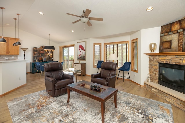 living area with ceiling fan, a stone fireplace, light wood-style flooring, lofted ceiling, and baseboards