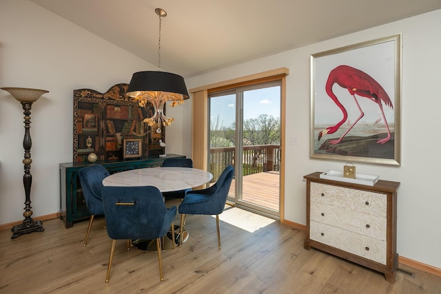 dining space featuring wood finished floors, baseboards, and vaulted ceiling