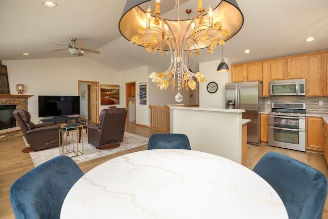 dining room with light wood-type flooring, a ceiling fan, recessed lighting, a stone fireplace, and vaulted ceiling