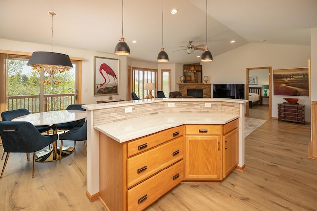 kitchen featuring open floor plan, lofted ceiling, a stone fireplace, light wood-style flooring, and ceiling fan