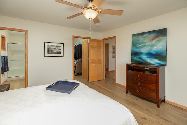 bedroom featuring light wood-type flooring, a spacious closet, baseboards, a closet, and ensuite bath