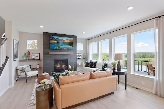 living area with baseboards, light wood-style flooring, a large fireplace, recessed lighting, and stairway