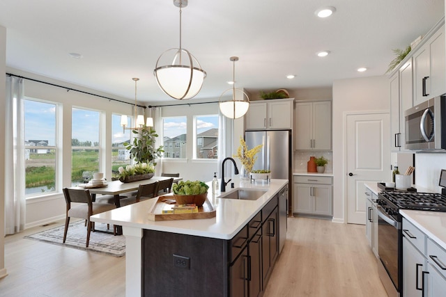 kitchen featuring stainless steel appliances, a sink, light wood finished floors, light countertops, and decorative backsplash