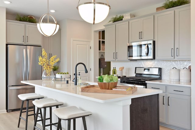 kitchen with appliances with stainless steel finishes, an island with sink, light countertops, tasteful backsplash, and recessed lighting