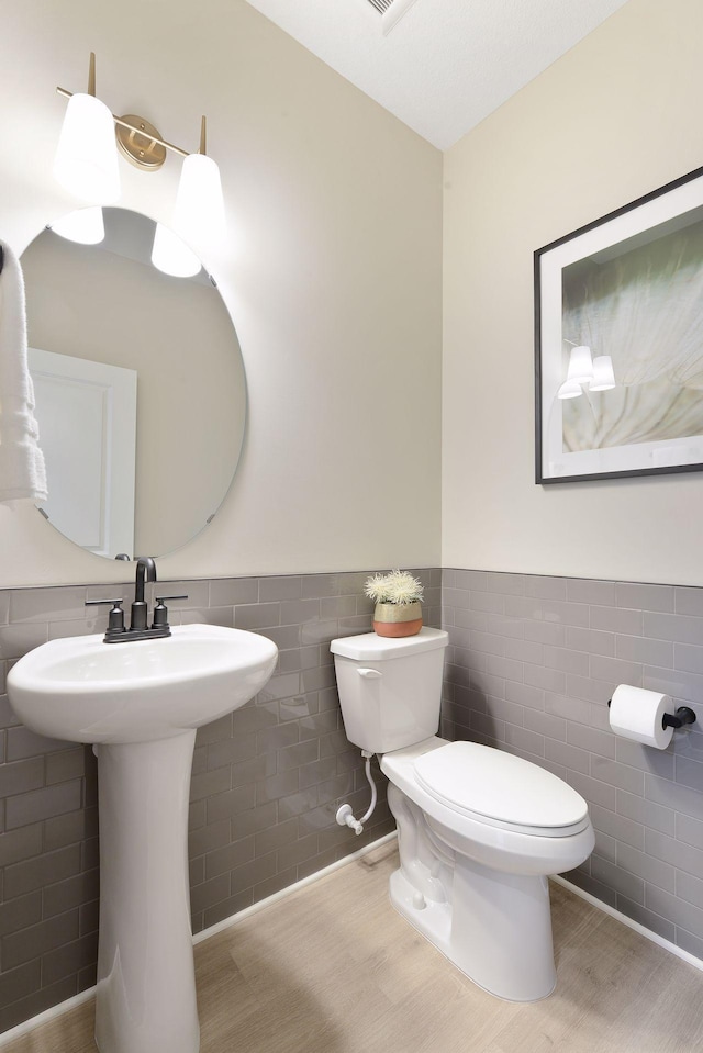 half bathroom featuring tile walls, toilet, wainscoting, and wood finished floors