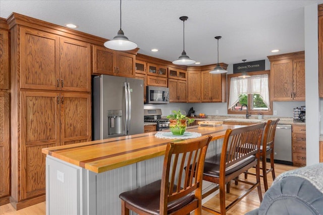 1704 156th St, Erin Prairie Twp, WI 54017 - kitchen featuring stainless steel appliances, brown cabinetry, glass insert cabinets, decorative light fixtures, and light wood-type flooring