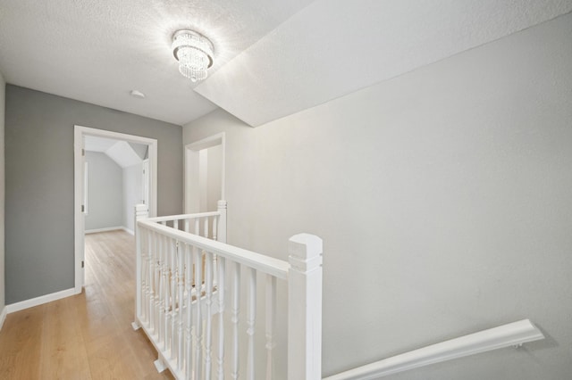 corridor with an upstairs landing, light wood-style flooring, baseboards, and a chandelier