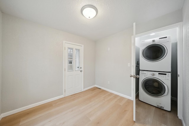 clothes washing area featuring estacked washer and dryer, light wood-style floors, baseboards, and a textured ceiling