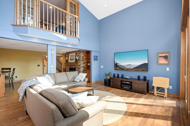 living area with high vaulted ceiling, baseboards, a brick fireplace, and wood finished floors
