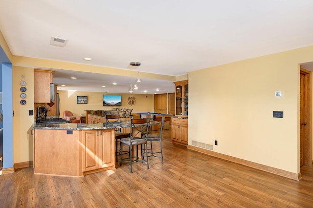 kitchen with a breakfast bar area, light wood-type flooring, glass insert cabinets, and recessed lighting