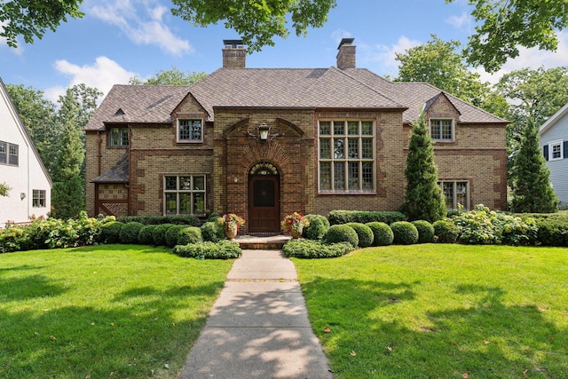 tudor home featuring brick siding, a chimney, and a front lawn