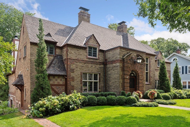 tudor-style house with brick siding, a chimney, and a front yard