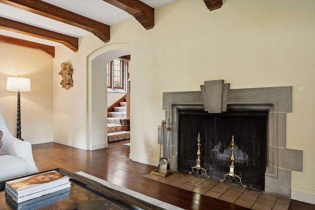 living room featuring arched walkways, stairway, baseboards, wood finished floors, and beamed ceiling