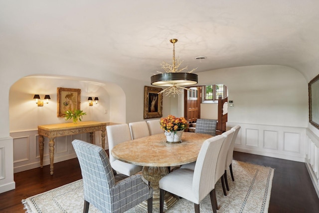 dining space featuring dark wood-style flooring, a decorative wall, wainscoting, and arched walkways
