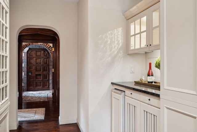 corridor featuring dark wood-type flooring, arched walkways, and baseboards