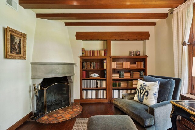 living area featuring beam ceiling, a large fireplace, wood finished floors, and baseboards