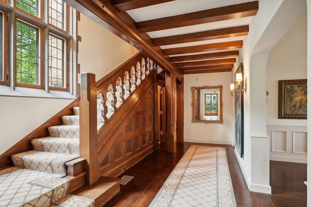 stairs with wood finished floors, beam ceiling, and arched walkways