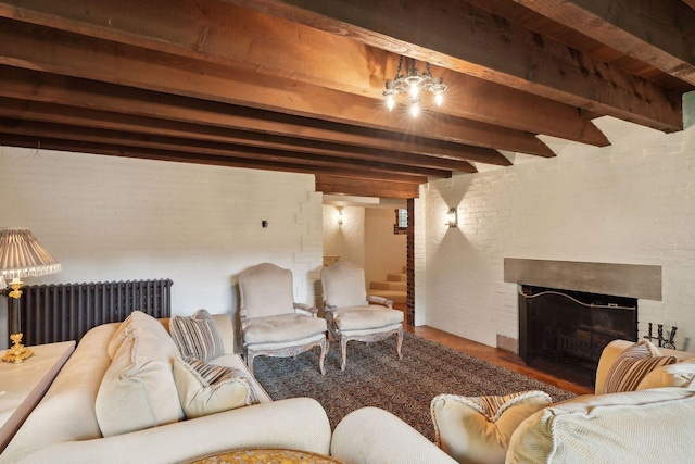 living room with radiator, wood finished floors, beamed ceiling, a fireplace, and brick wall