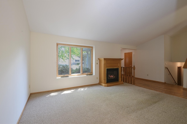 unfurnished living room featuring carpet floors, lofted ceiling, a glass covered fireplace, and baseboards