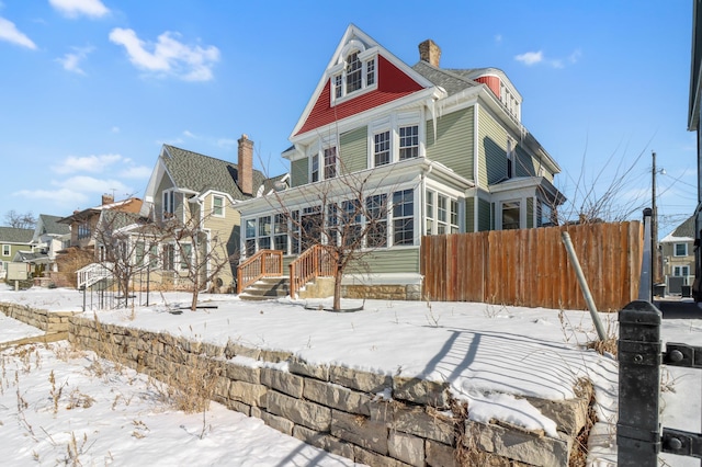 snow covered house with fence, a chimney, and a sunroom