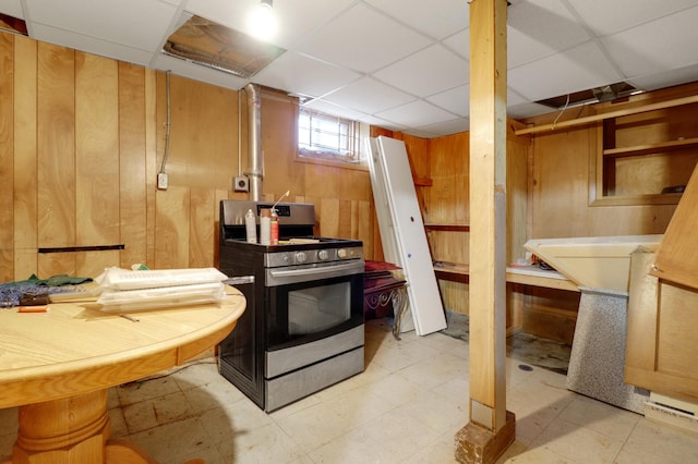 kitchen with gas range, wooden walls, light floors, and a paneled ceiling